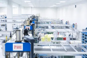 A bright, sterile manufacturing facility where workers in white protective suits are operating machinery to produce and stack yellow thermoformed food packaging.
