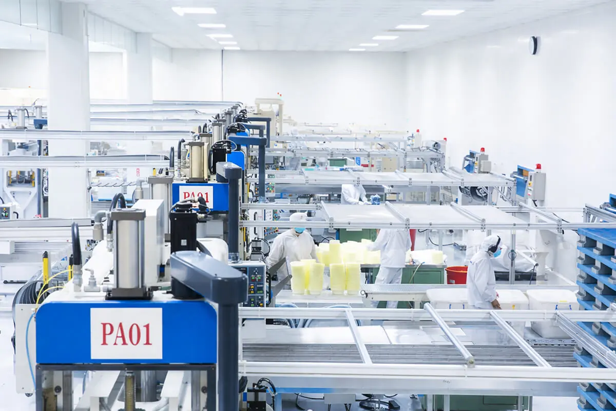 A bright, sterile manufacturing facility where workers in white protective suits are operating machinery to produce and stack yellow thermoformed food packaging.
